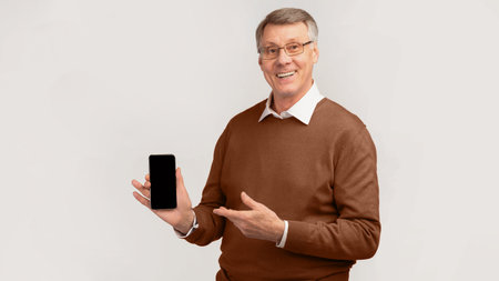 Senior Man Showing Smartphone Standing Over Gray Background, Mockup, Panoramaの写真素材