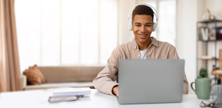 Young man learning online at home with laptop and headphones during daytime