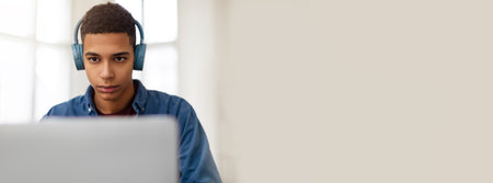 Young man focused on computer work while wearing headphones at home