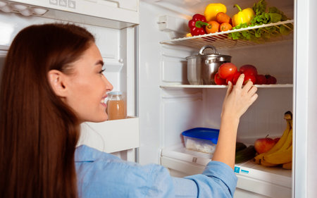 Happy girl taking organic vegetables from fridge at homeの写真素材