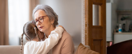 Grandmother comforts granddaughter during emotional moment at homeの写真素材
