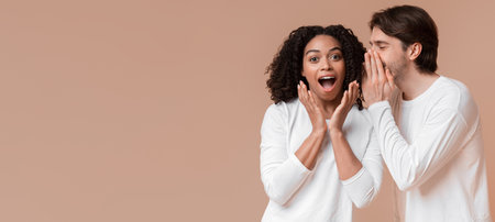 Young man sharing secret with his shocked black girlfriend