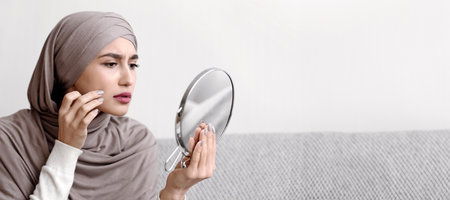Muslim Girl In Hijab Looking In Round Mirror And Touching Skinの写真素材