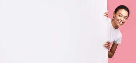 Girl Peeking Out Of Blank Poster Standing Over Pink Backgroundの写真素材