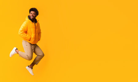 Joyful afro guy in warm jacket jumping in the air