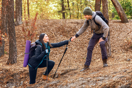 Handsome hiker helping his girlfriend uphill in forestの写真素材