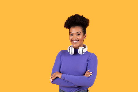 Young woman in a purple top and headphones, smiling against yellow
