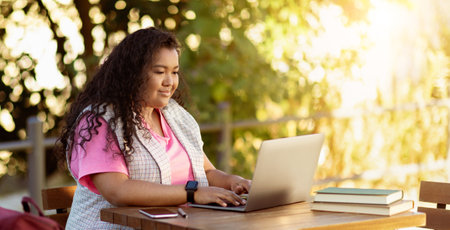 Young woman working on a laptop outdoors in a sunny park setting