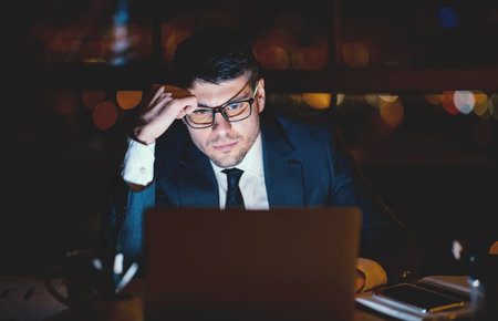 Serious Office Worker At Laptop Thinking Working Overnight At Workplaceの写真素材