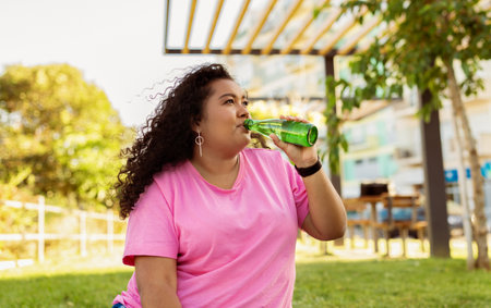 Woman enjoying a refreshing drink in a sunny park setting during the afternoonの写真素材