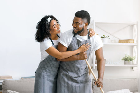 Happy black couple doing household chores together, mopping floor and huggingの写真素材