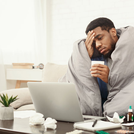 Sick african-american man working on laptop at homeの写真素材