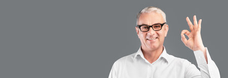 Smiling elderly man gesturing ok sign at grey studio