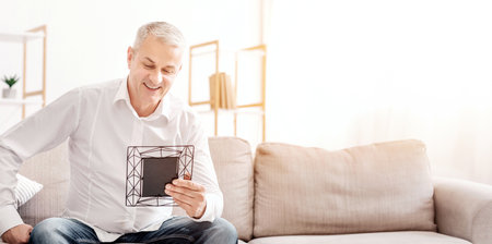 Cheerful man sitting on couch holding photo frameの写真素材