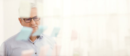 Elderly manager looking at sticky notes on windowの写真素材