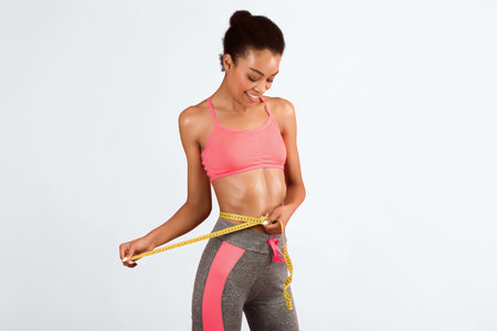 Slim African American Girl Measuring Waist Over Pink Studio Backgroundの写真素材