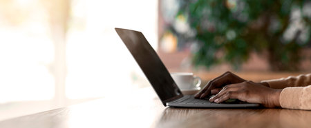 Hands of black girl typing on laptop keyboard, cafe interior