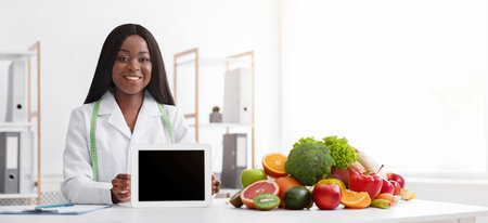 Smiling afro woman nutritionist showing empty tablet screen at clinicの写真素材