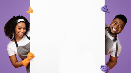 Smiling black couple of cleaners peeking out behind white advertising boardの写真素材