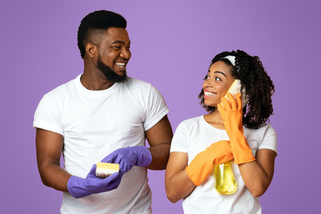 Crazy Cleaning. Joyful couple using sponges like cellphones, having fun during tidyingの写真素材