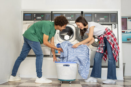 Couple doing laundry together in a modern laundromat on a sunny dayの写真素材