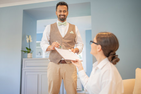 A man in a vest hands a clipboard to a woman in a white shirtの写真素材