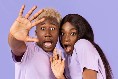 Portrait of black couple with scared or shocked faces on lilac background
