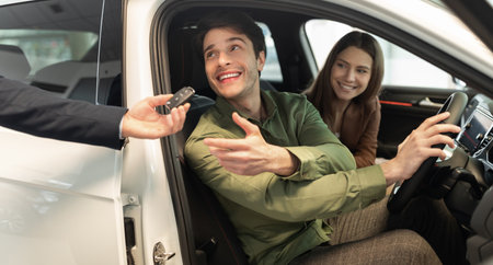 Happy millennial couple taking car key from auto salesman, sitting inside modern automobile at dealership, panoramaの写真素材