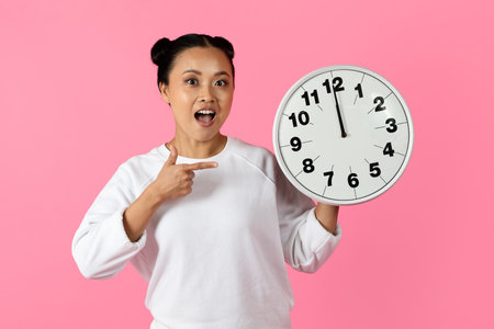 Woman happily pointing at clock on pink background in bright indoor setting