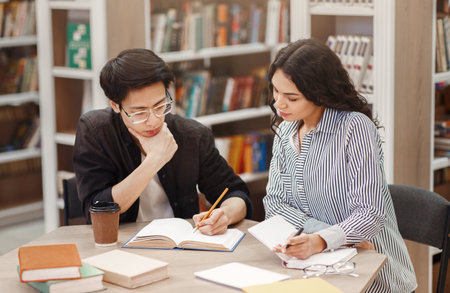 Two concentrated multiracial students learning at libraryの写真素材