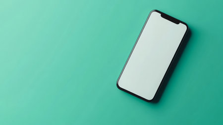 Smartphone lying on a mint green surface with a blank screen in a minimalist settingの素材
