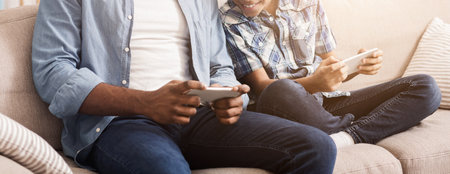 Cheerful Black Boy And His Dad Playing Video Games On Smartphones