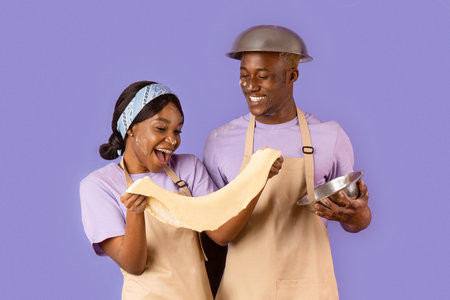 Romantic cooking times. Young black couple with dough baking on lilac background