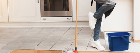 Happy young woman cleaning kitchen floor dancing with mop
