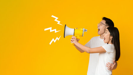 Young asian couple shouting in megaphone over yellow backgroundの写真素材