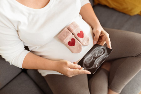 Expecting mother looking at ultrasound while holding baby booties on her belly