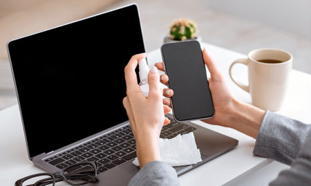 Woman disinfects smartphone and laptop in workplace
