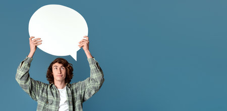 Attractive teenage guy holding speech bubble with blank space for your design, turquoise backgroundの写真素材