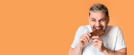 Man sweet tooth happily bites chocolate isolated on yellow backgroundの写真素材