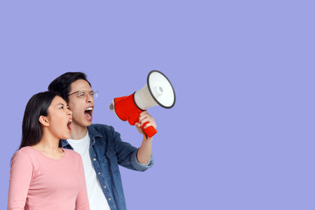 Emotional young asian couple with megaphone screaming towards copy spaceの写真素材