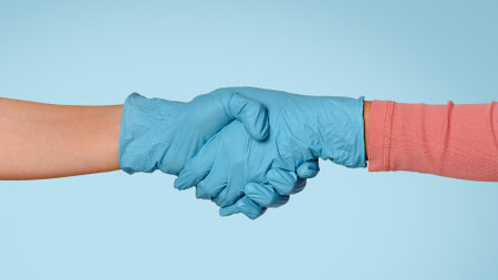 Handshake of two people wearing blue medical gloves, closeupの写真素材