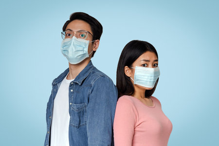 Afraid Asian Couple In Protective Medical Masks Over Light Studio Backgroundの写真素材
