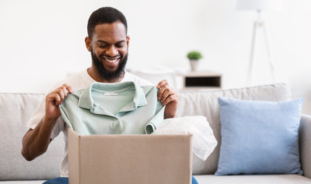 African Man Receiving Clothes Unpacking Box Holding T-Shirt At Home
