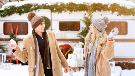 Young couple enjoying a snowball fight outside a cozy camper during winterの写真素材