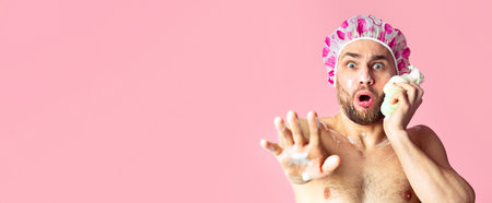 Scared guy in shower cap rubs his face with spongeの写真素材