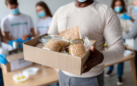 Senior black man holding box with donations food, cans and packages with grains and pasta, croppedの写真素材