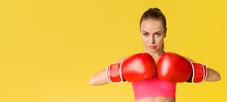 Portrait Of Confident Young Woman Wearing Boxing Gloves On Yellow Backgroundの写真素材