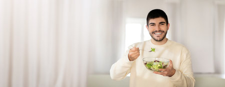 Young man enjoying a fresh salad in a bright indoor setting during daytimeの写真素材
