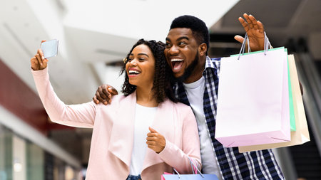 Joyful Black Couple Taking Selfie On Smartphone After Successful Shopping In Mallの写真素材