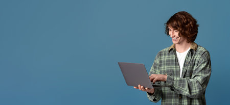 Remote communication. Handsome young guy with laptop chatting online, working or studying on color backgroundの写真素材